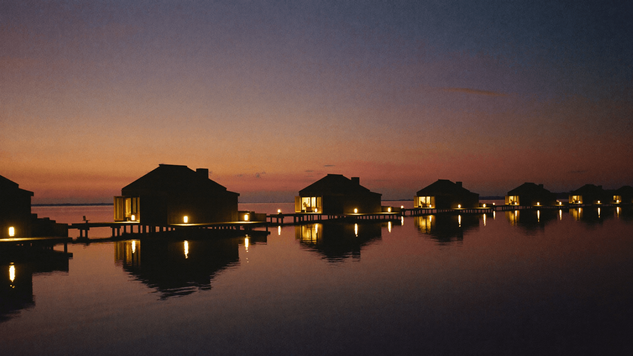 Overwater villas glowing with lantern light on a calm lagoon at dusk
